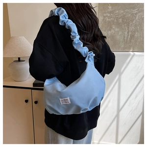 Détail du sac croissant bleu clair avec bandoulière plissée et étiquette tendance