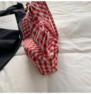 Detail of red and white checkered fabric tote bag with fine stitching on white bedding