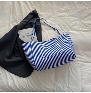 Detail view of blue and white striped canvas tote bag with a front pocket on white fabric