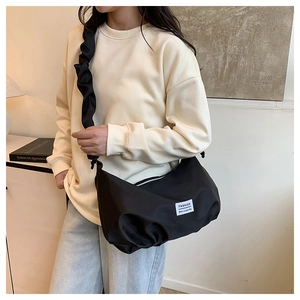 Détail d'un sac bandoulière en nylon noir avec bandoulière plissée et étiquette fashion