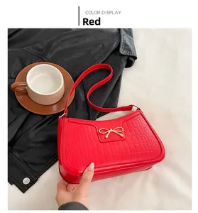 Detail of red faux leather shoulder bag with crocodile pattern and golden bow accent