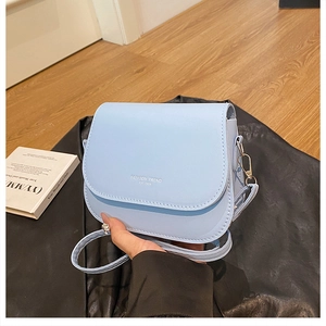 Detailed view of light blue saddle bag featuring magnetic clasp and fashion trend text