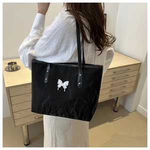 Detail view of a black pleated tote bag with a white butterfly ornament on the side