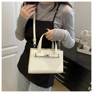 Close-up of white litchi pattern leather bag with silver turn-lock and black strap
