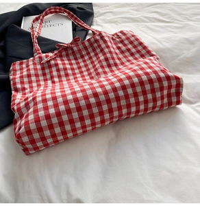 Close-up of red and white gingham tote bag with a decorative bow on a white bed