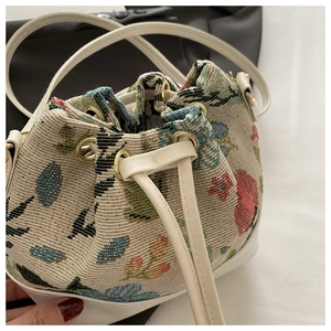 Close-up of drawstring bucket bag featuring floral jacquard fabric and white leather trim