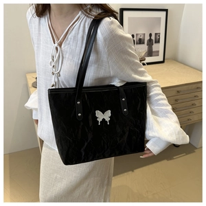 Detail of black tote bag with silver butterfly emblem and pleated texture on shoulder
