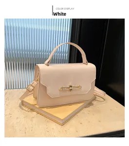 Elegant beige small square handbag with golden hardware buckle displayed on a book