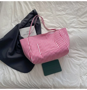 Detail of red and white striped canvas tote bag with a front pocket and long shoulder straps
