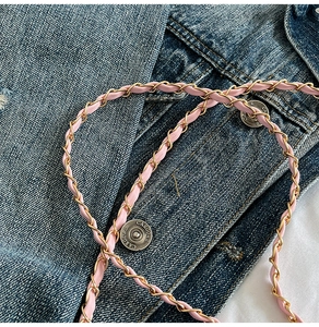 Detail of pink leather interwoven with gold metal chain strap on denim background