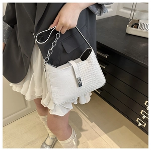Detail of white crocodile embossed handbag with metallic twist lock and silver chain strap
