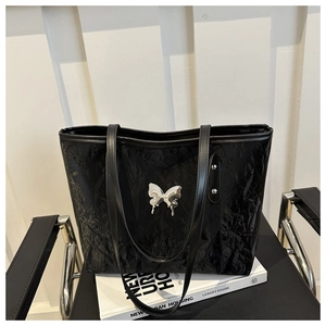 Detail of black tote bag with wrinkled texture and silver butterfly ornament on leather chair
