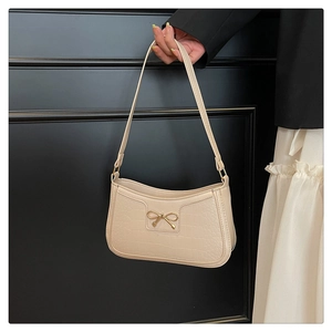 Detail of beige faux crocodile underarm bag featuring a gold bow metallic ornament