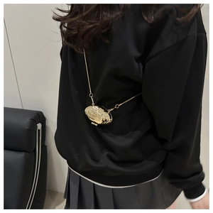 Mini sac coquillage doré en métal avec fine chaîne porté par un mannequin en tenue noire
