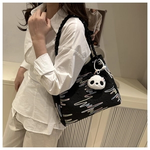 Detail of black tote bag with wave embroidery and cute panda plush keychain on model