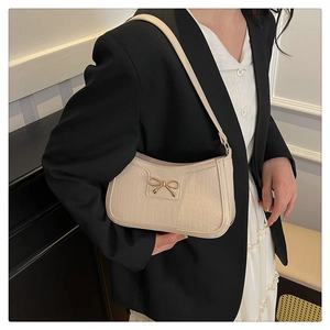 Detail of cream faux crocodile underarm bag with an elegant golden bow clasp on the front