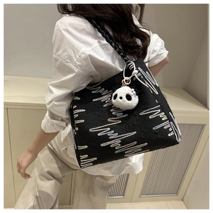 Detailed view of black bucket bag with colorful embroidery and plush panda charm
