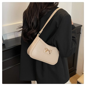 Detail of off-white crocodile-embossed shoulder bag with gold bow clasp on a model