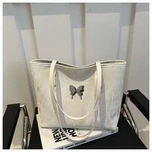 Detailed view of white tote bag with silver liquid metal butterfly buckle on leather texture
