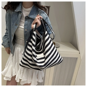 Detail of striped canvas tote bag with black lace trim held by a model in casual outfit