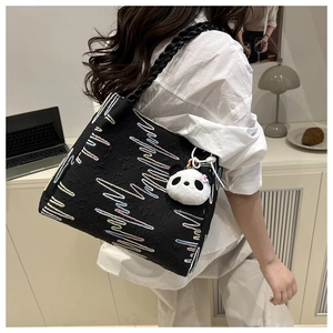 Detail of black embroidered tote bag with colorful wave patterns and panda charm accessory