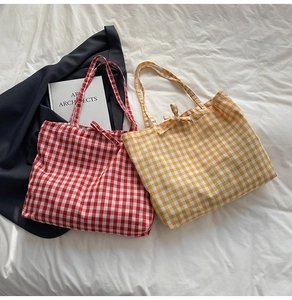 Detailed view of canvas tote bags featuring red and yellow plaid patterns with bow ties