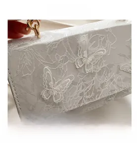 Close-up of white lace embroidery and butterfly pattern on a fashion square clutch