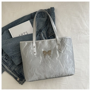 Detail of silver metallic tote bag with crinkled texture and metal butterfly badge