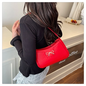 Detail of red crocodile pattern shoulder bag with a gold metal bow and zipper closure