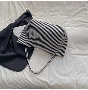 Detailed top view of striped canvas tote bag on white bedding with aesthetic lifestyle props