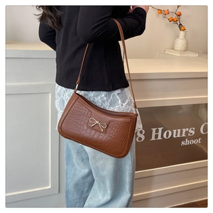 Gros plan du sac bandoulière marron motif croco avec un nœud doré métallique