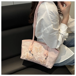 Pink lace shoulder bag with 3D butterfly embroidery worn by model on a bench