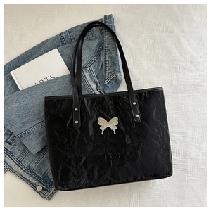 Detail of black tote bag featuring metallic butterfly buckle and pleated texture
