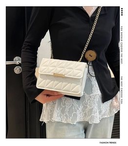 Detail of white quilted handbag with geometric pattern and gold chain strap on model