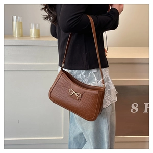 Detail of a brown crocodile pattern shoulder bag with a gold bow buckle on a model