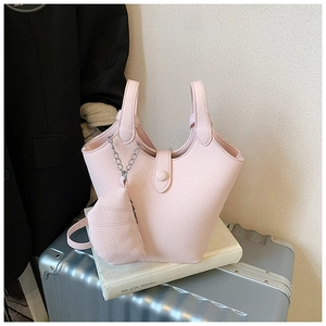 Pink lychee grain leather bucket bag with silver chain detail on travel background