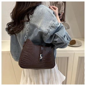 Detail of dark brown crocodile texture shoulder bag with metallic chain on model