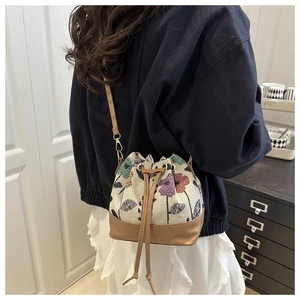 Detail of floral tapestry drawstring bucket bag with brown leather base and thin strap