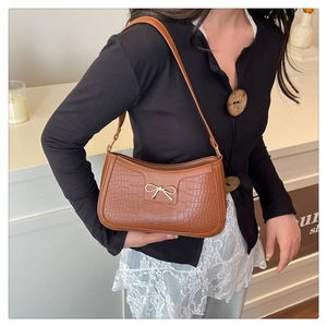 Close-up of brown croc-effect shoulder bag featuring a gold bow metallic buckle
