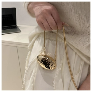Detail of a mini gold shell-shaped bag with a metallic hammered texture and snake chain