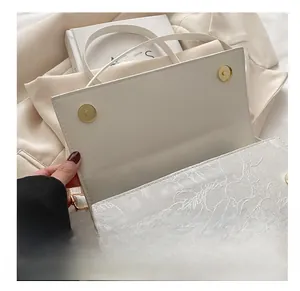Detail of white lace embossed square bag with golden magnetic snap buttons and strap