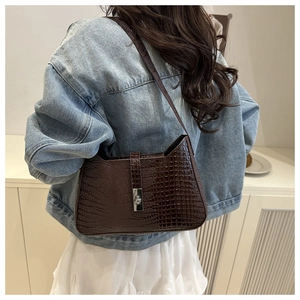 Detail of dark brown crocodile embossed shoulder bag worn over a denim jacket