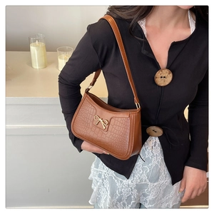 Detail of a brown croc-embossed hobo bag with a gold bow buckle on a black sweater