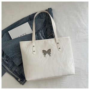 Detailed view of white crinkled tote bag featuring a metallic butterfly and rivets