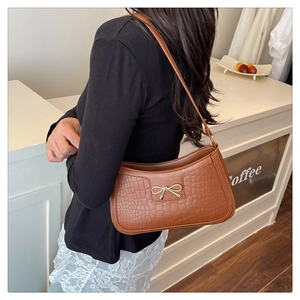 Détail de la texture crocodile et boucle nœud doré sur le sac à bandoulière marron