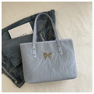 Detailed view of blue tote bag featuring crinkled texture and silver butterfly ornament