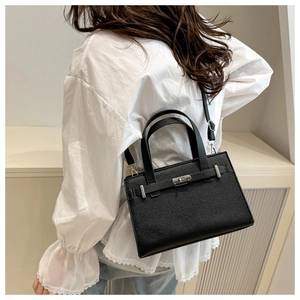 Close-up of black lychee grain leather tote bag with silver turn-lock and crossbody strap