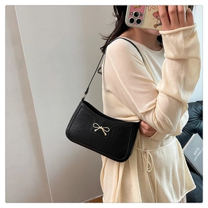 Detail of black faux crocodile texture underarm bag featuring a gold metal bow charm