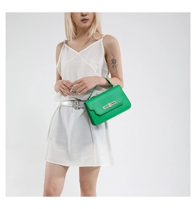 Detail of vibrant green handbag with gold oval clasp held by a model in white dress