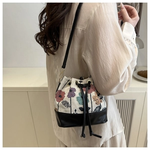 Detail of embroidered floral bucket bag featuring beige fabric and black leather strap